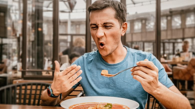 A man wincing and eating spicy red soup