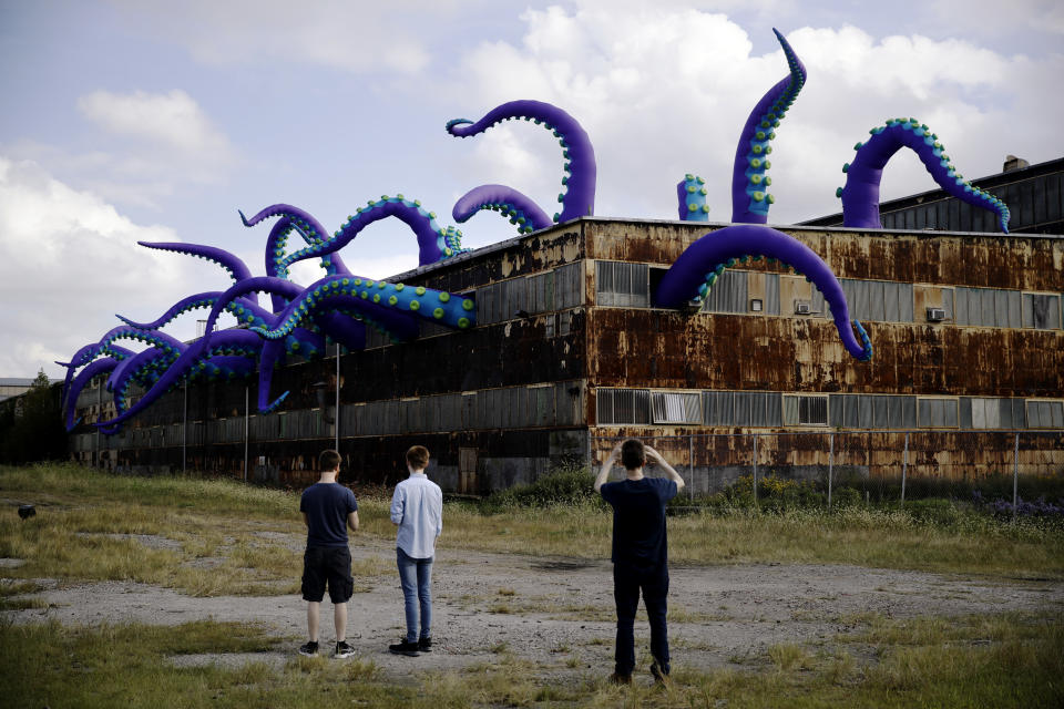 An inflatable sculpture entitled "Sea Monsters HERE" extends from a rusting warehouse called Building 61 at the Navy Yard in Philadelphia, Tuesday, Oct. 9, 2018. The installation was created by UK-based artists Filthy Luker and Pedro Estrellas. The former military base is free and open to the public. (AP Photo/Matt Rourke)