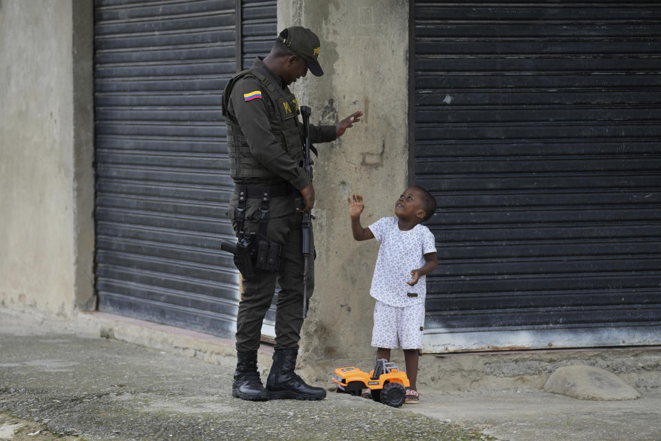 A police officer greets a toddler in a neighborhood that has criminal gangs in Buenaventura, Colombia, Thursday, Aug. 17, 2023. Programs for the young people that gangs recruit are planned in Buenaventura and other cities, but the country's most powerful armed groups have grown stronger, according to experts, and bloodshed between rival groups has skyrocketed. (AP Photo/Fernando Vergara)