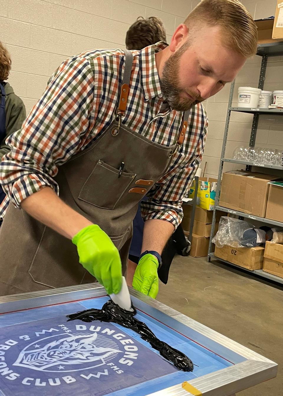 Print shop teacher Brian Fogarty loads the print screen with black water-based ink. A student will spread the ink across the screen creating a custom T-shirt at Farragut Middle School. March 20, 2024.