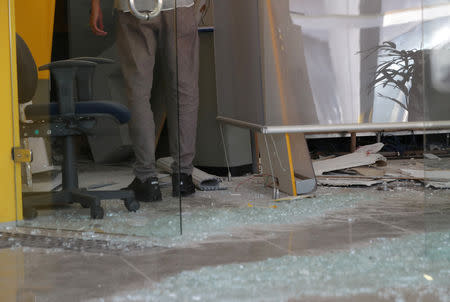 An employee stands near broken glass at a damaged branch of Banco do Brasil after a gang caused an explosion in a part of the bank in an attempted robbery, in Guararema, near Sao Paulo, Brazil April 4, 2019. REUTERS/Amanda Perobelli