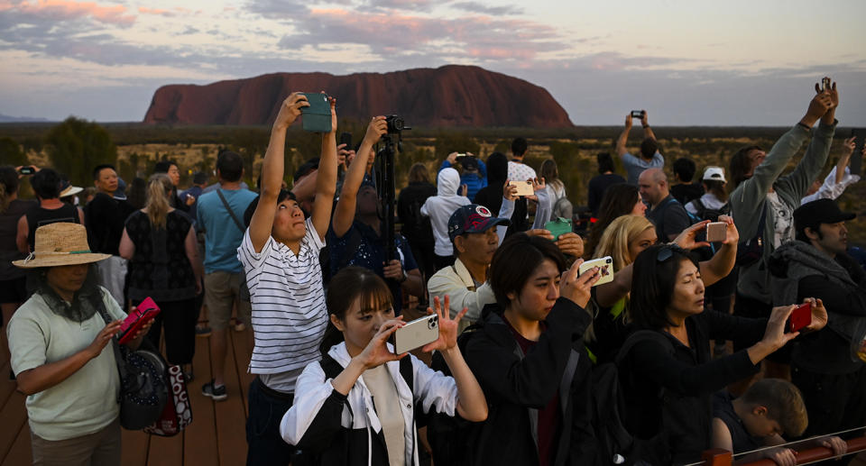 Tourists are seen taking photographs of the rising sun near Uluru, also known as Ayers Rock at Uluru-Kata Tjuta National Park in the Northern Territory, Saturday, October 12, 2019. Climbing Uluru will be banned starting from October 26, 2019. (AAP Image/Lukas Coch) NO ARCHIVING