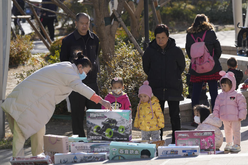 A vendor shows toys to young children on the street of Beijing, China, Tuesday, Dec. 7, 2021. Chinese leaders on Friday, Dec. 10, 2021 promised tax cuts and support for entrepreneurs next year to shore up slumping economic growth after a campaign to rein in surging corporate debt caused bankruptcies and defaults among real estate developers. (AP Photo/Ng Han Guan)