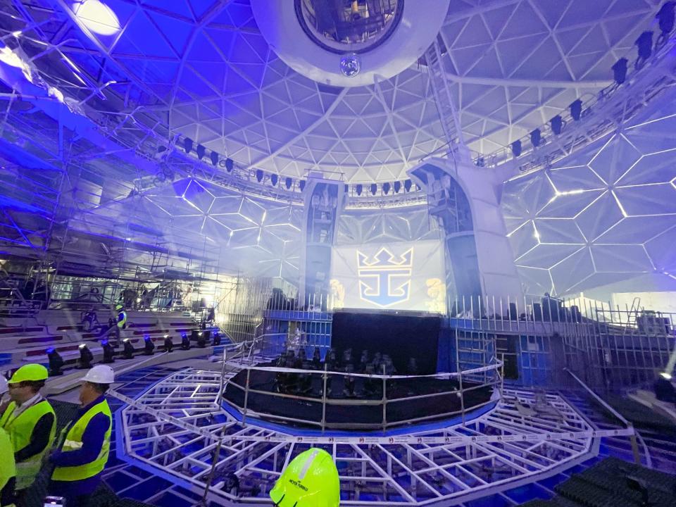 People in high-visibility jackets and hard hats standing in a large circular room that has Royal Caribbean's logo on one of the white walls.