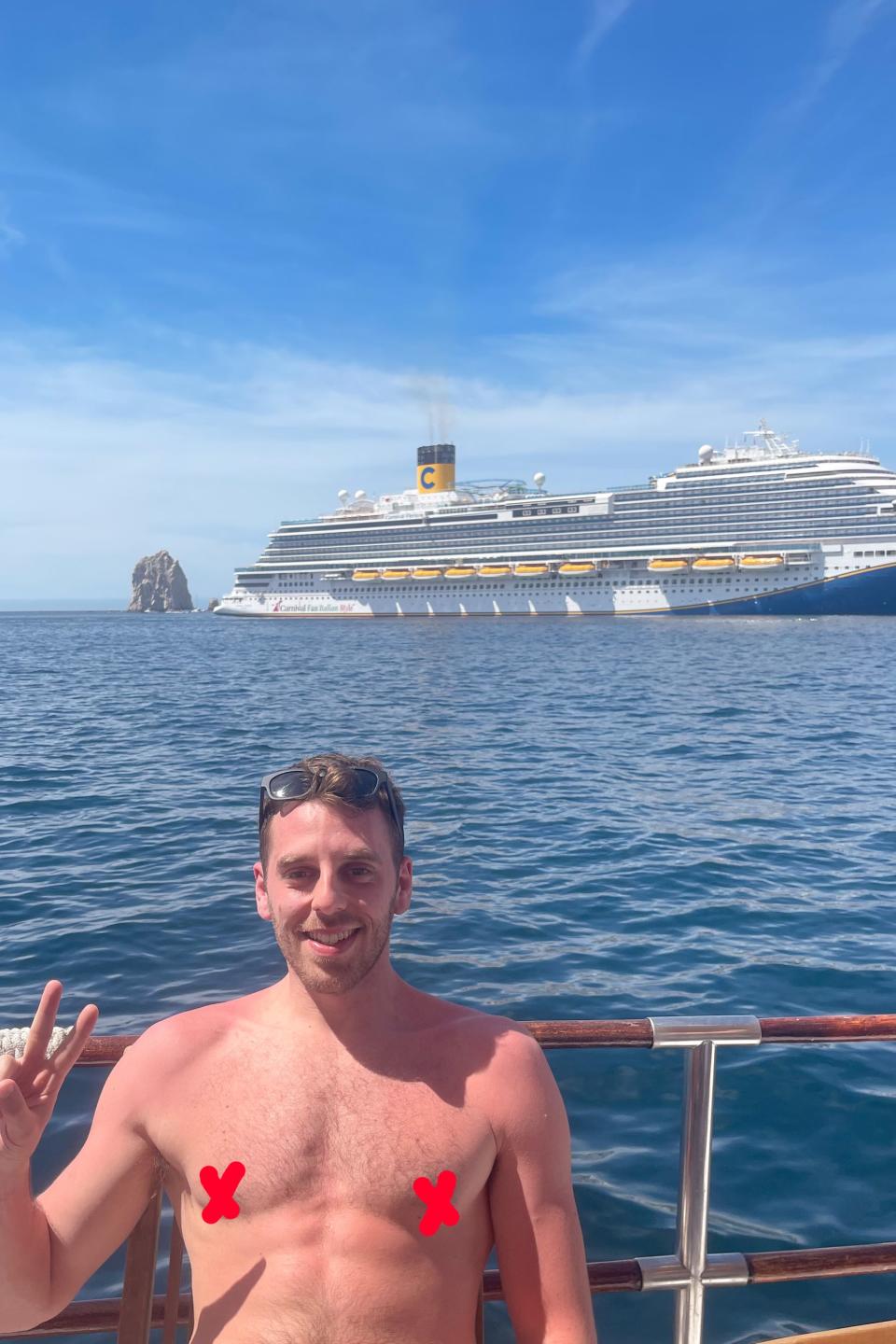 Man giving a peace sign on a boat with a cruise ship in the background