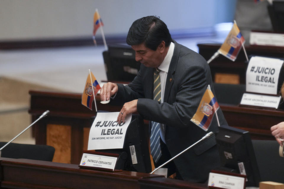 A lawmaker places a sign that reads in Spanish "Illegal trial" during a session at the National Assembly where opposition lawmakers seek to try President Guillermo Lasso over embezzlement accusations in Quito, Ecuador, Tuesday, May 16, 2023. (AP Photo/Dolores Ochoa)