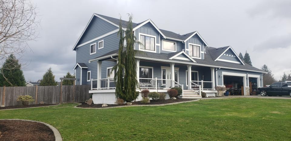 A spacious clapboard home with steps up to a porch set on a verdant lawn.