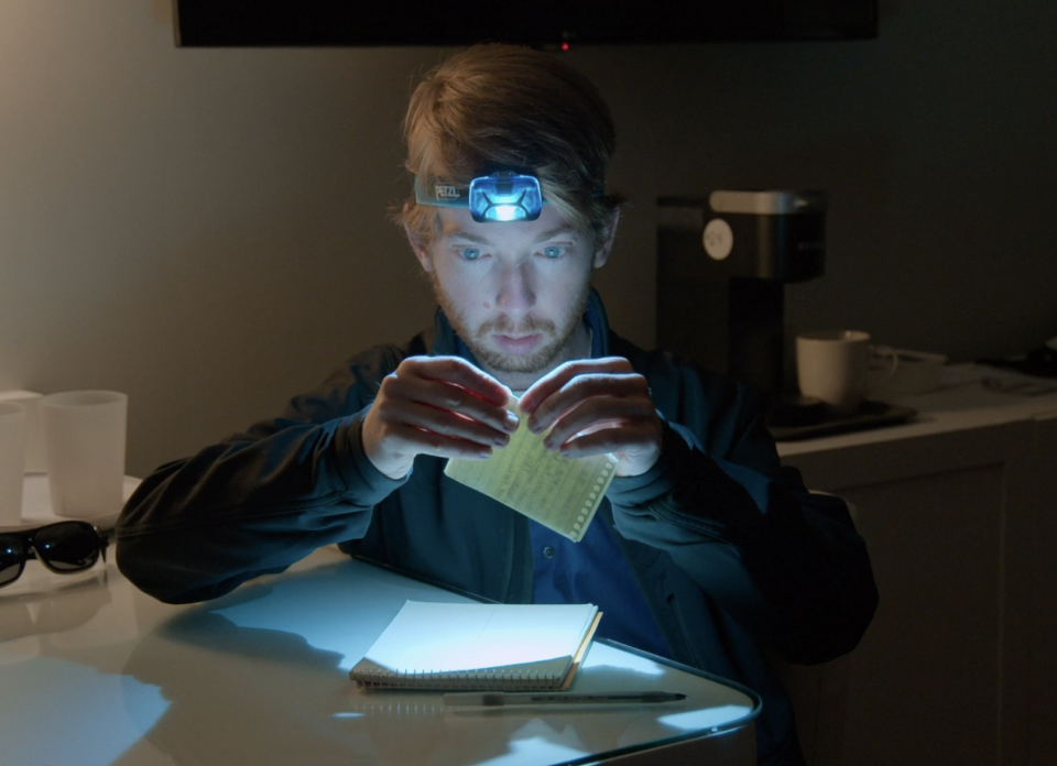 he's wearing a headlamp as he folds up a piece of paper in the hotel room