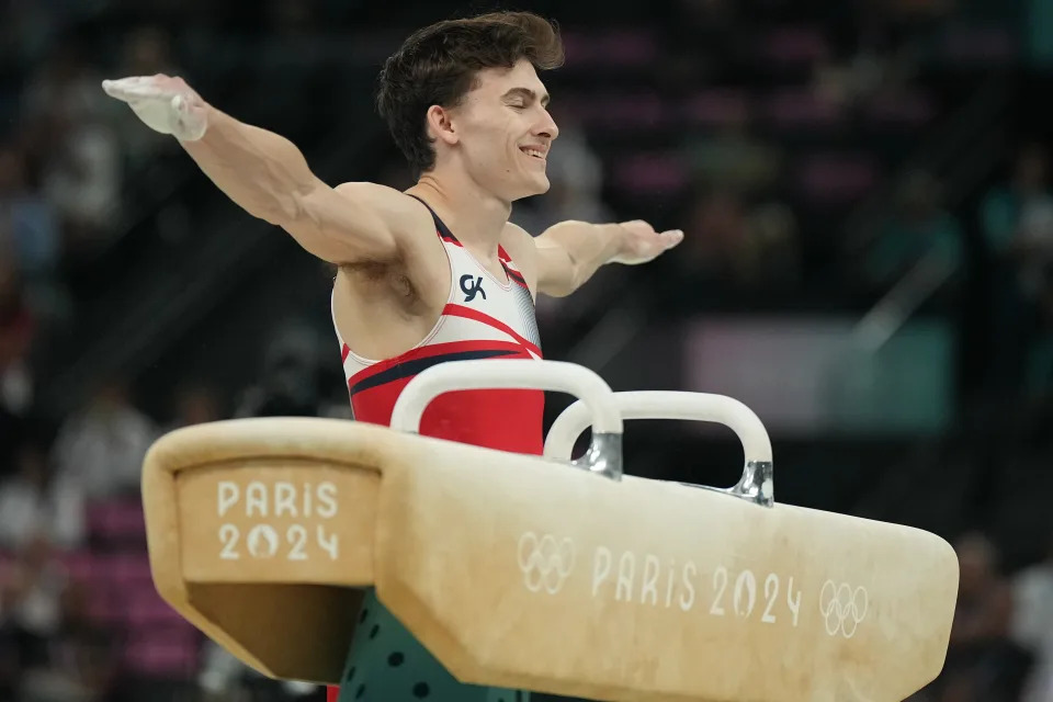 Stephen Nedoroscik stands next to the pommel horse with his arms outstretched.