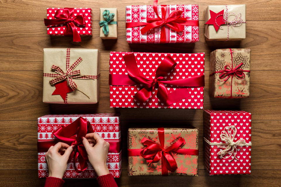 Woman fixing a bow on beautifuly wrapped vintage christmas presents on wooden background, view from above