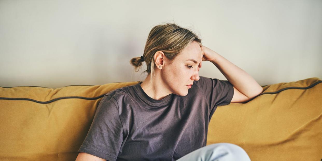 a young woman is sitting on the yellow couch at home with her head in her hands