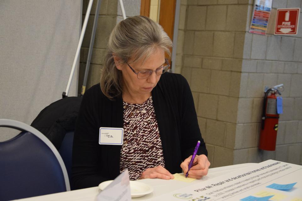 Thea Murray writes on a sticky note to add to a solutions and barriers board during a public input meeting hosted by the Michigan Department of Environment, Great Lakes, and Energy on Dec. 12, 2023.