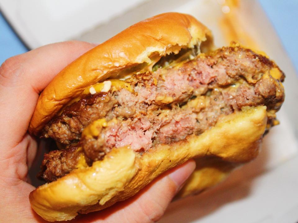 bitten into shake shack double cheeseburger in paper wrapping on blue background