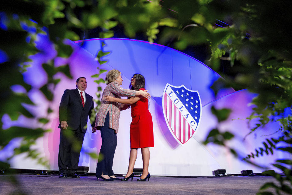 In this July 14, 2016 photo Democratic presidential candidate Hillary Clinton, accompanied by then-LULAC President Roger C. Rocha, Jr., left, hugs University of Texas student Dreamer Lizeth Urdiales, right, as she arrives to speaks at the 87th League of United Latin American Citizens National Convention at the Washington Hilton in Washington. LULAC, the nation's oldest Latino civil rights organization, voted Saturday, Sept. 26, 2020, to postpone its planned national convention in Albuquerque, N.M., in 2021 over uncertainty caused by COVID-19. (AP Photo/Andrew Harnik, File)