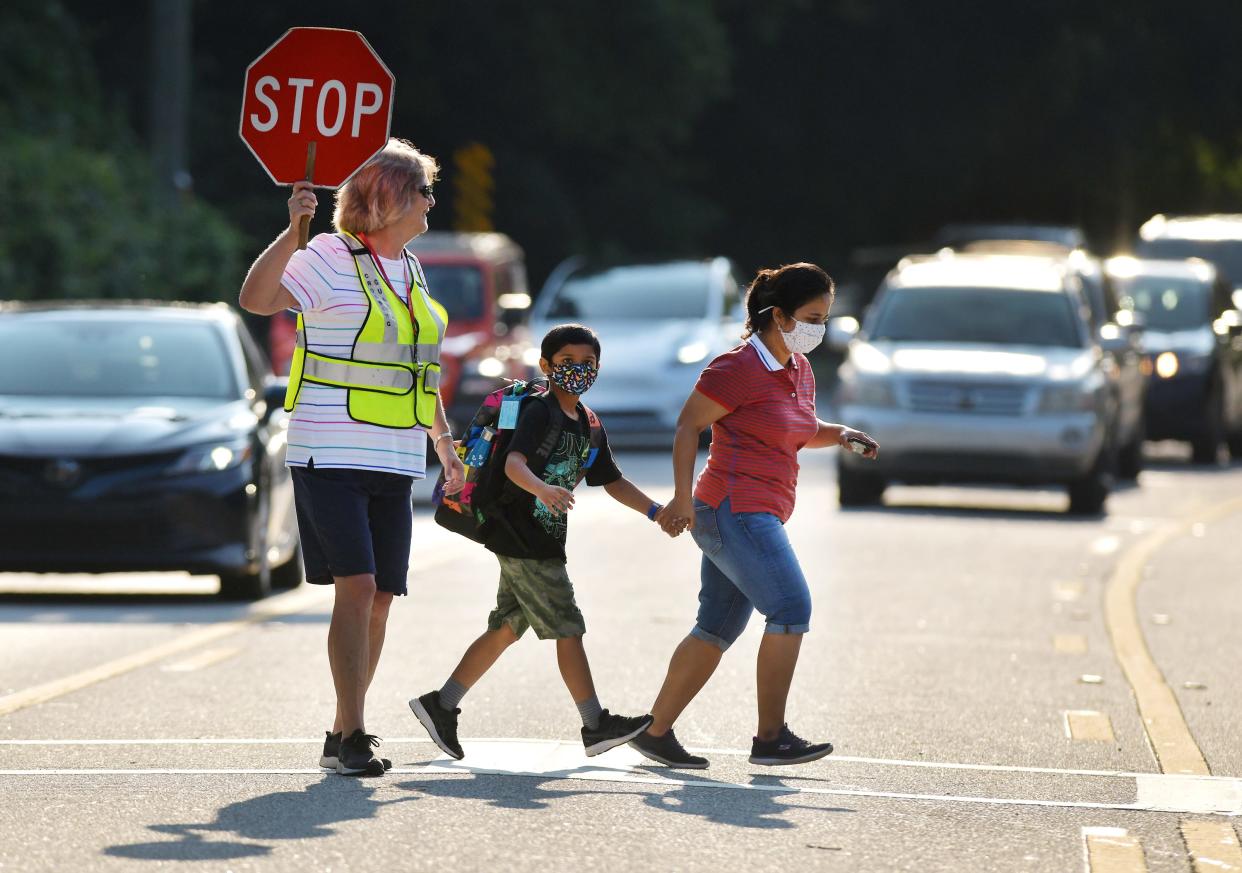 Crossing guard Kelly Linder helps a masked mother and son across Loretto Road as they make their way to Loretto Elementary School for the first day of school last year.