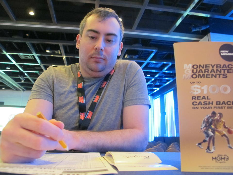 Mike Heusser, of Middletown, Conn., checks off bets he planned to make on the NCAA basketball tournament, Thursday, March 21, 2019, at the Borgata casino in Atlantic City. College basketball fans are lining up at casinos and racetracks, and furiously tapping smartphone screens to get down bets on the March Madness college basketball tournament, in many states where it is legal for the first time. (AP Photo/Wayne Parry)