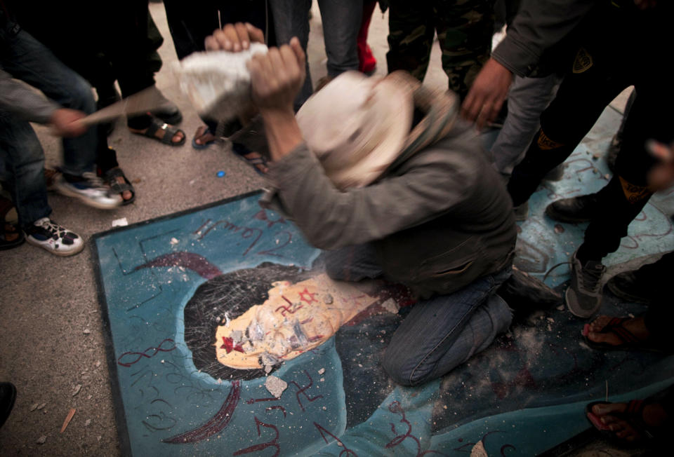 FILE - In this Feb. 26, 2011, file photo, a Libyan man uses a stone to hit a defaced billboard of Libyan leader Moammar Gadhafi during a demonstration against the regime in the city of Tobruk, eastern Libya. Libya has been plunged into chaos again, with forces loyal to a polarizing military commander marching on the capital and trading fire with militias aligned with a weak U.N.-backed government. (AP Photo/Kevin Frayer, File)