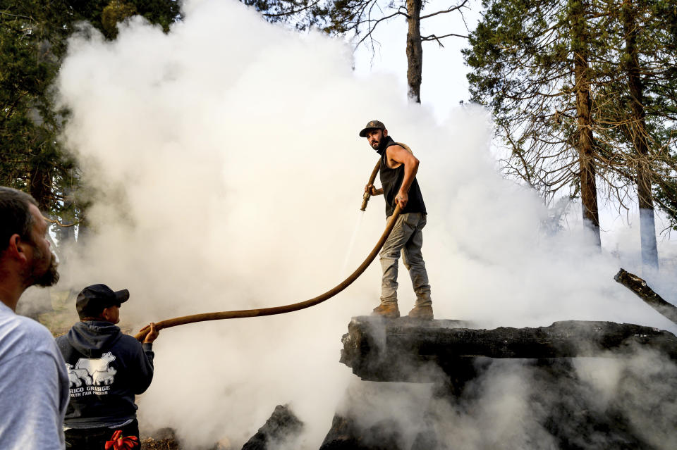 Derrick Harlan sprays water on a burn pile, Wednesday, Oct. 25, 2023, in Paradise, Calif. He was clearing a property of dead wood and flammable vegetation to meet defensible space requirements Paradise adopted following the Camp Fire. (AP Photo/Noah Berger)