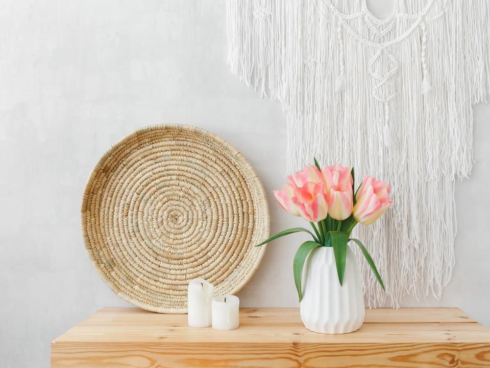 White ceramic vase, bouquet of pink tulip flowers, wicker tray, candles, and macrame