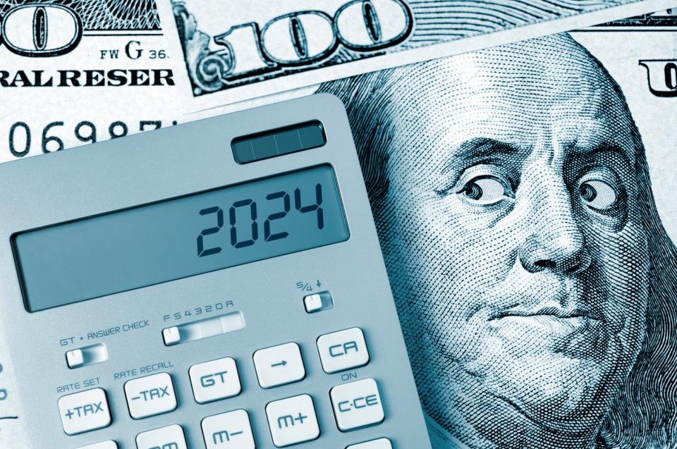 An up-close view of Ben Franklin on a one hundred dollar bill staring at a calculator displaying the numbers, 2024.
