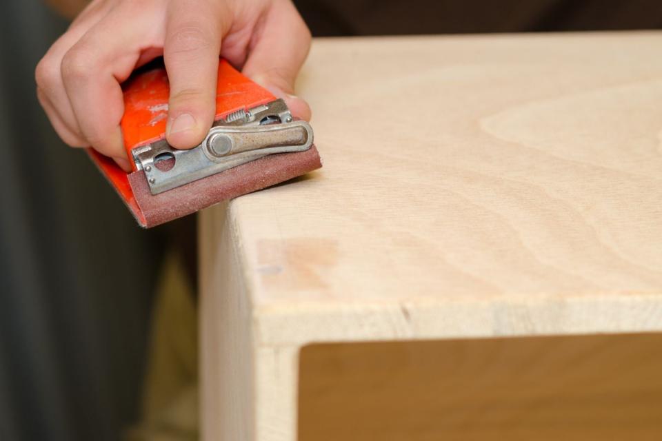 A close up of a person using a tool to refinish a piece of furniture.