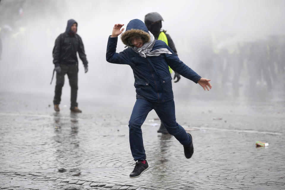 A demonstrator runs away after being sprayed with a water canon in clouds of teargas as yellow vest protesters clash with riot police on the famed Champs Elysees avenue in Paris, France, Saturday, Jan. 12, 2019. Authorities deployed 80,000 security forces nationwide for a ninth straight weekend of anti-government protests. (AP Photo/Thibault Camus)