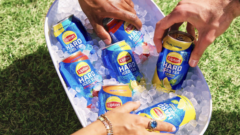 Three hands grabbing Lipton hard iced tea from cooler