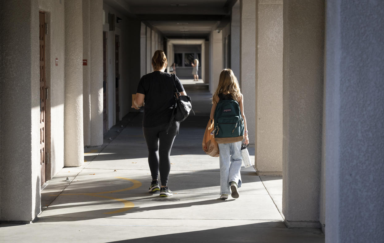 A student and parent, from behind, walk down a covered sidewalk at what appears to be a school.
