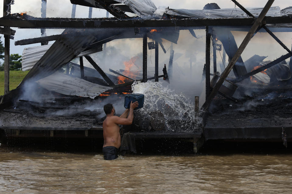 An illegal miner throws water at one of the more than 60 dredging barges that were set on fire by officers of the Brazilian Institute of the Environment and Renewable Natural Resources, IBAMA, during an operation to try to contain illegal gold mining on the Madeira river, a tributary of the Amazon river in Borba, Amazonas state, Brazil, Sunday, Nov. 28, 2021. Hundreds of barges belonging to illegal miners had converged on the river during a gold rush in the Brazilian Amazon prompting IBAMA authorities to start burning them. (AP Photo/Edmar Barros)