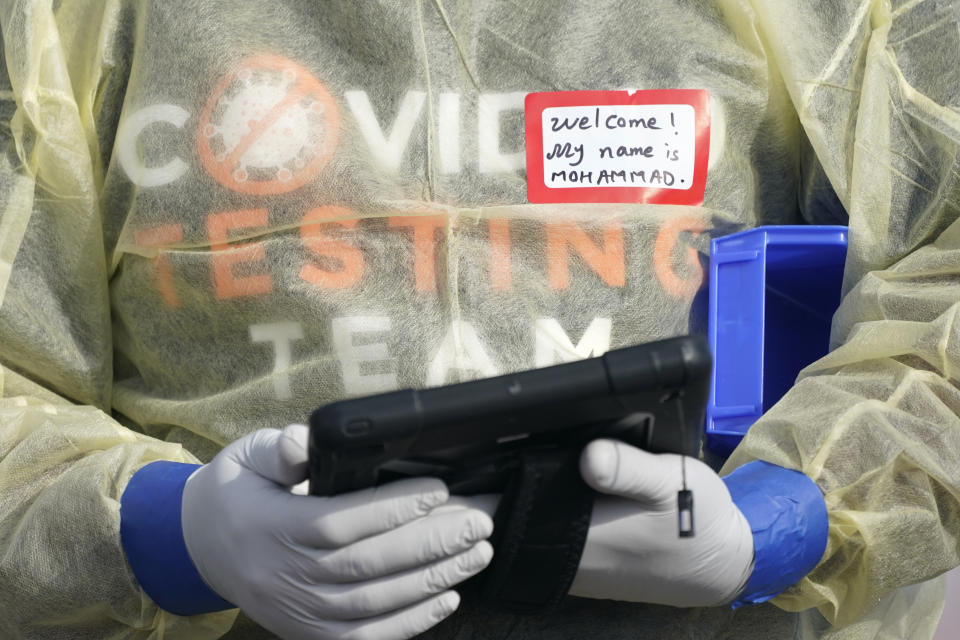 A worker wearing gloves, and other PPE holds a tablet computer as he waits to check people in, Wednesday, Oct. 28, 2020, at a King County coronavirus testing site in Auburn, Wash., south of Seattle. State health officials say that a new COVID-19 report released Wednesday shows an increase in coronavirus cases and hospitalizations throughout Washington state, and if not brought under control, officials said the spike could jeopardize progress toward reopening schools, strain the health care system and increase risks during the holiday season. (AP Photo/Ted S. Warren)