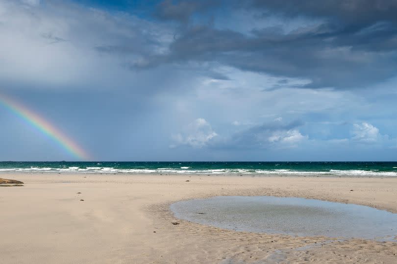 Rainbow forming over sea and Crossapol Beach on Isle of Tiree, Inner Hebrides, Scotland.