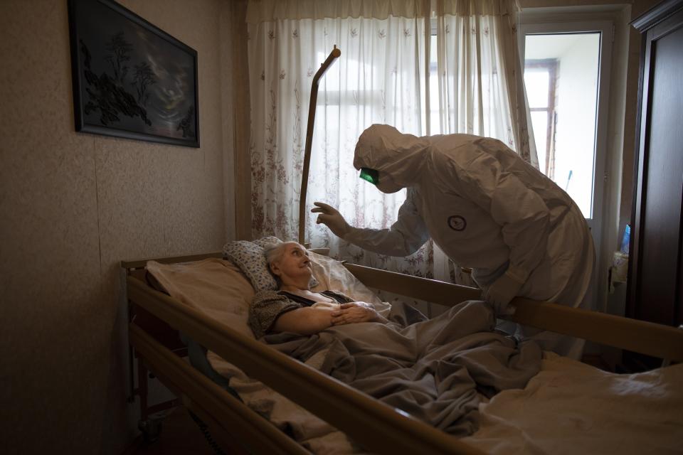 In this photo taken on Monday, June 1, 2020, In this photo taken on Monday, June 1, 2020, Father Vasily Gelevan wearing a biohazard suit and gloves to protect against the coronavirus, blesses Lyudmila Polyak, 86, suspected of having coronavirus at her apartment in Moscow, Russia. In addition to his regular duties as a Russian Orthodox priest, Father Vasily visits people infected with COVID-19 at their homes and hospitals. (AP Photo/Alexander Zemlianichenko)
