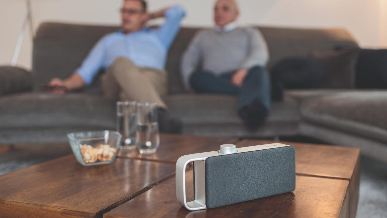  faller OSKAR speaker on a coffee table, with two men in the background watching TV 