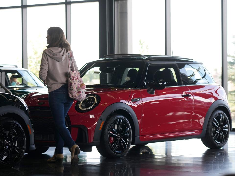 A woman walks by two cars inside a showroom.