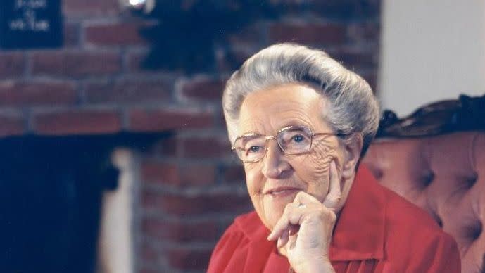 corrie ten boom sitting in a chair while resting her head in her left hand and holding a book