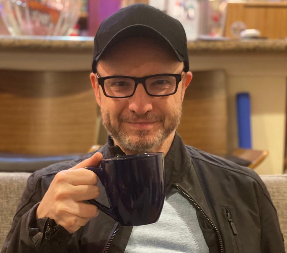 Man wearing black baseball cap and glasses holding up a mug.