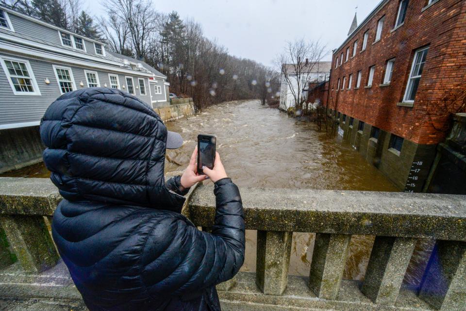 Cassidy Doolittle of Wilmington, Vt., takes a photo of the water marker on the side of a building in downtown Wilmington as the Deerfield River gets to 14 feet high on Monday, Dec. 18, 2023, after a heavy storm dropped a couple of inches of rain. (Kristopher Radder/The Brattleboro Reformer via AP)