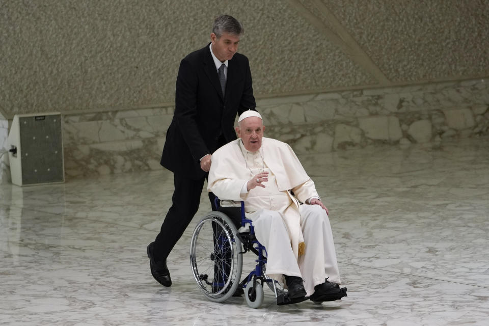 Pope Francis arrives in a wheelchair to attend an audience with nuns and religious superiors in the Paul VI Hall at The Vatican, Thursday, May 5, 2022. Francis, 85, has been suffering from strained ligaments in his right knee for several months. He revealed he recently received some injections to try to relieve the pain, but he has continued to struggle to walk and stand. (AP Photo/Alessandra Tarantino)