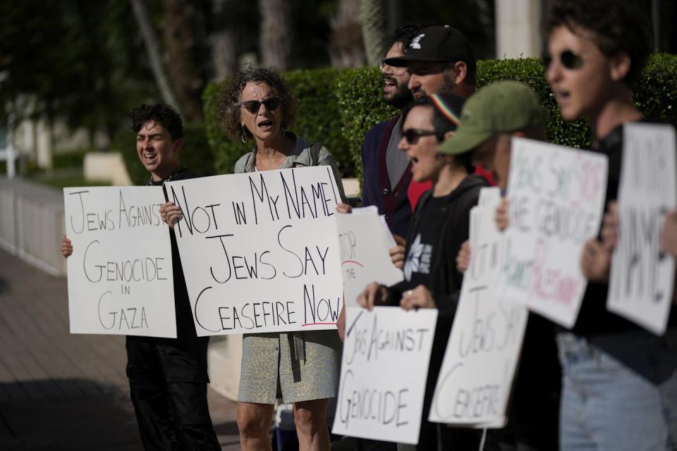 A handful of people appear to chant while holding handwritten signs and standing on a sidewalk.