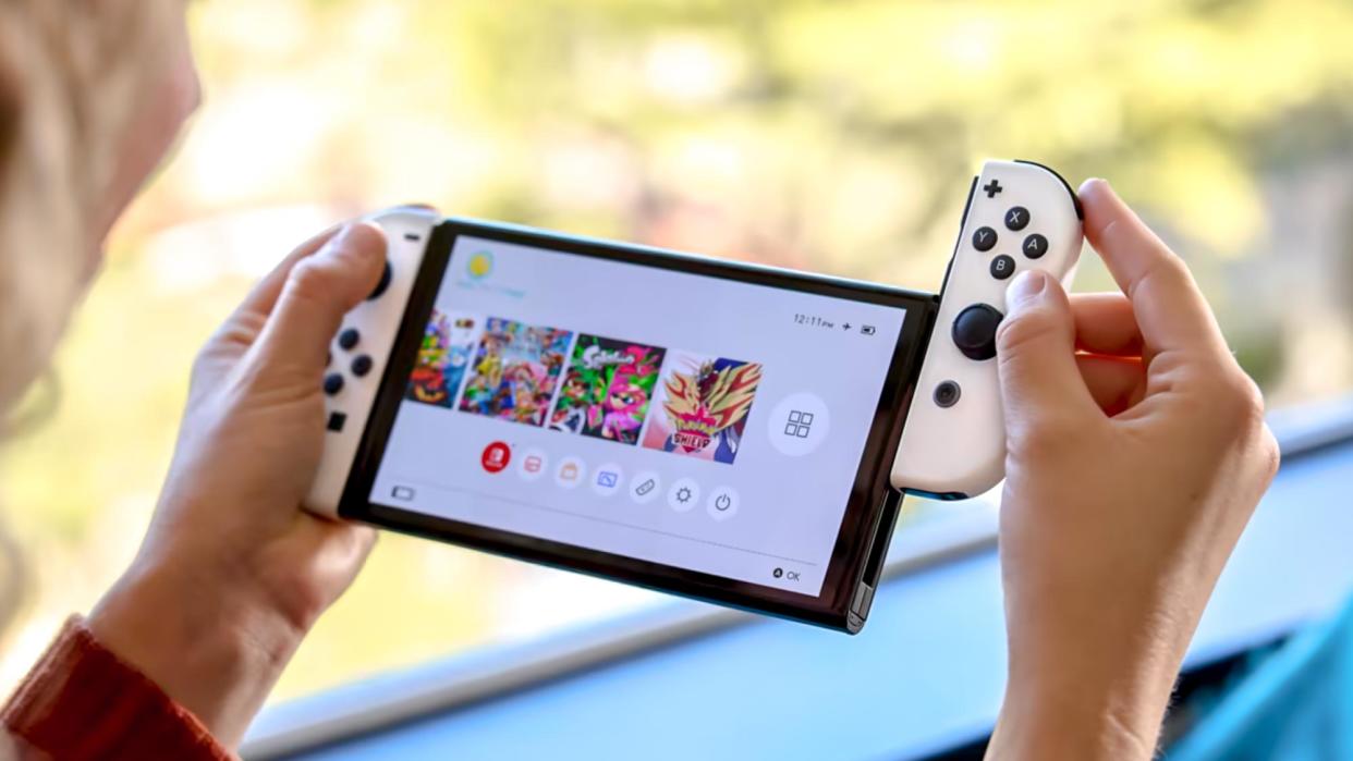  Nintendo Switch OLED held between two hands with one of the JoyCons being slid off. 