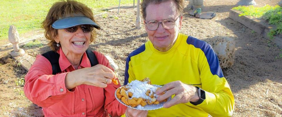 Cheerful senior couple sharing funnel cake with powdered sugar at autumn country fair in Missouri, USA