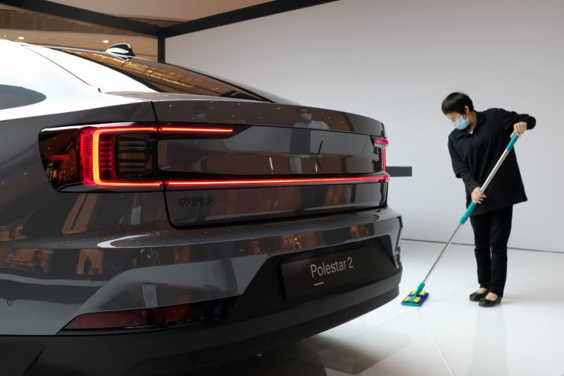 Worker cleans the floor near a Polestar 2 electric sedan at a shopping mall in Shanghai