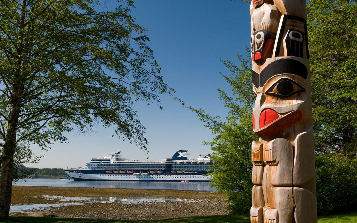 A totem pole in Sitka National Park with cruise ship in background - iStock