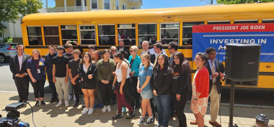 State and local officials and other dignitaries pose for a group photo with Roosevelt Middle School 8th graders outside of their school on Friday, as one of New Bedford's new electric school buses sits parked in the background.