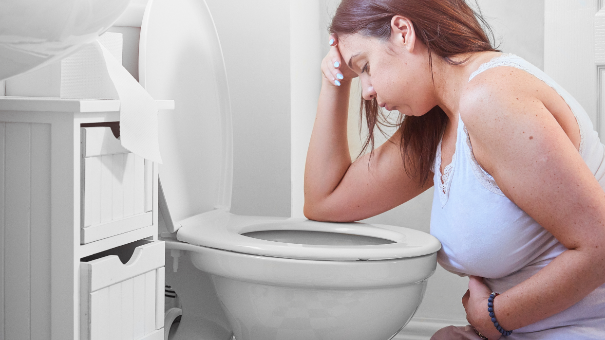  Woman knelt at the toilet with her head in her hands looking like she is going to be sick 