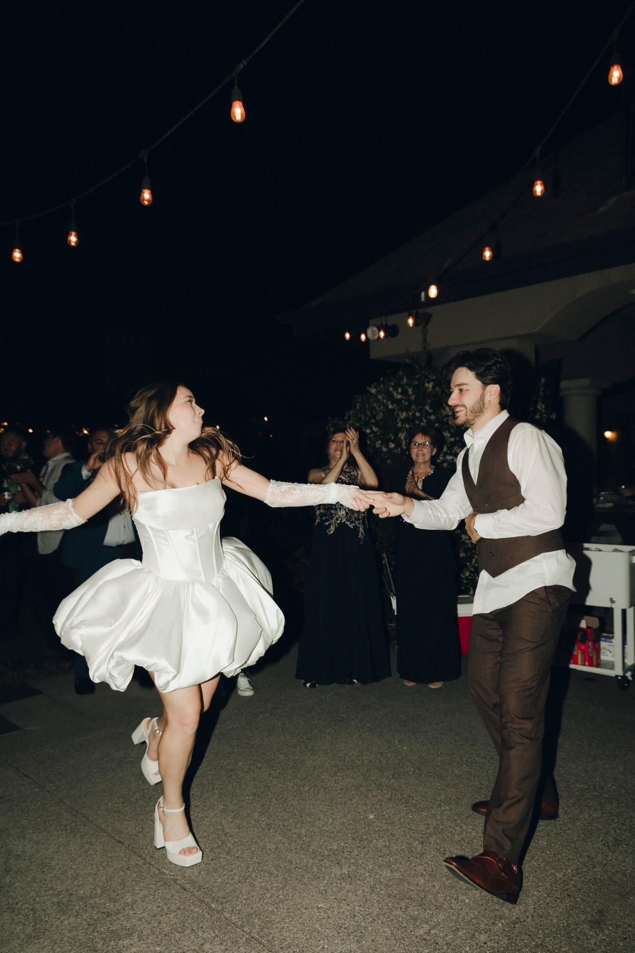 A bride and groom dance together at their wedding. She wears a short dress.