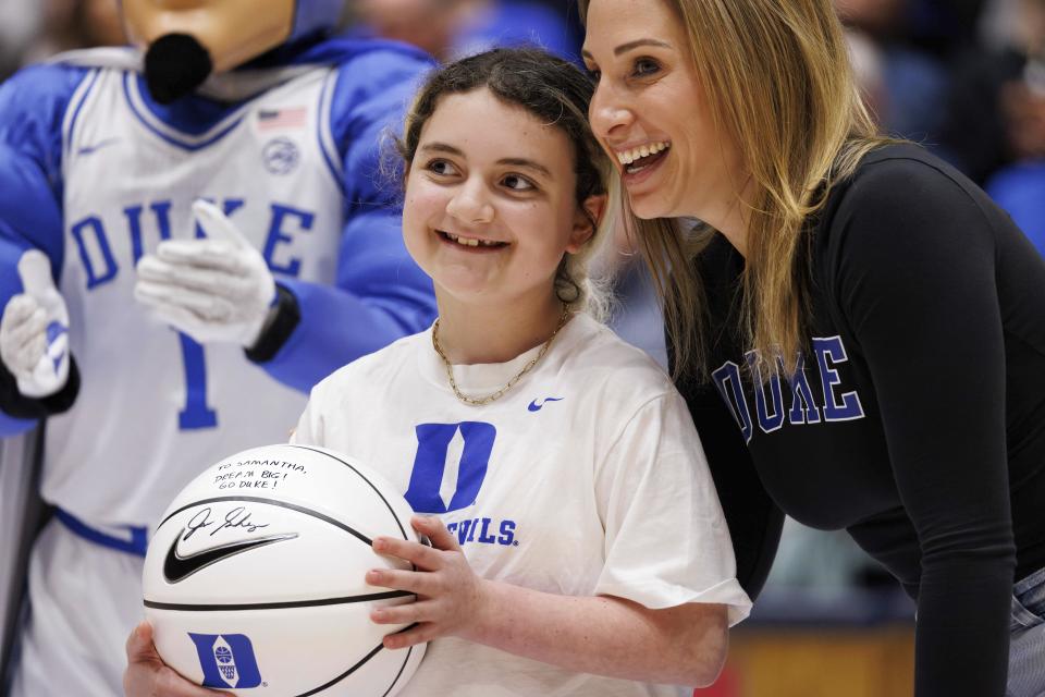 Marcelle Scheyer, right, wife of Duke coach Jon Scheyer, smiles after presenting a basketball signed by coach Scheyer to Samantha DiMartino, left, as an honoree of the Scheyer Family Kid Captain Program, which recognizes patients and families of Duke Children's Hospital, during a timeout in an NCAA college basketball game between Duke and Louisville in Durham, N.C., Wednesday, Feb. 28, 2024. (AP Photo/Ben McKeown)
