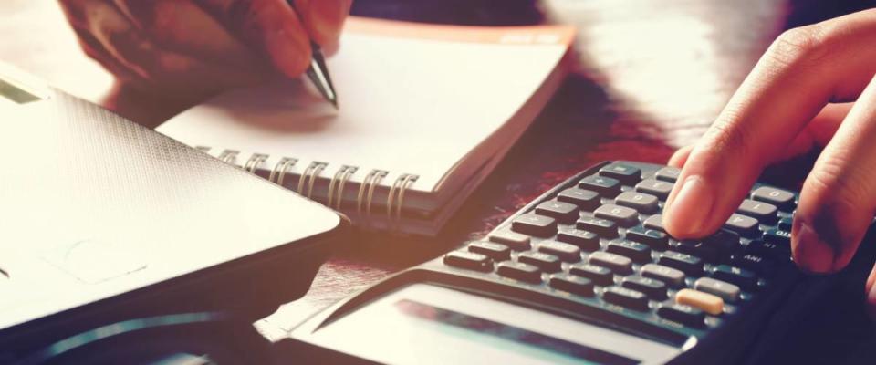 Close up woman hand using calculator and writing make note with calculate about cost at home office.