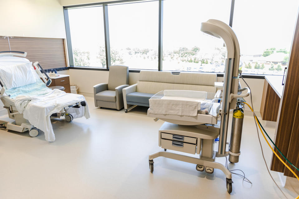 Hospital room with an empty bed, medical equipment, and a couch near the window. No people are visible