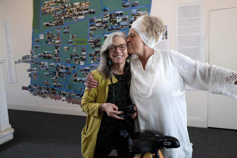 Artist Sumaya Evans, right, gives a kiss to writer and activist Judy Branfman in the entrance to Beyond Baroque gallery by a map she created as part of an exhibit titled "Where Has All The (affordable) Housing Gone?" on Friday, Nov. 3, 2023, in the Venice Beach area of Los Angeles. Word spread about her photo project and Branfman started hosting community meetings where residents could share their experiences with evictions that forced them to move out of the area and, in some cases, into homelessness. (AP Photo/Richard Vogel)